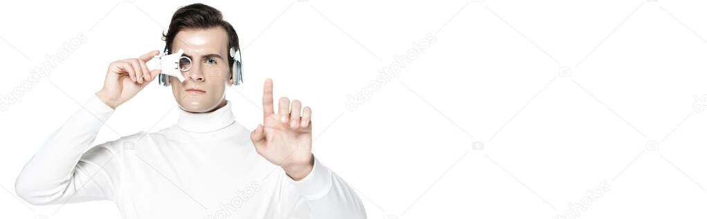 Cyborg man in digital eye lens and headphones looking at camera while touching something isolated on white, banner