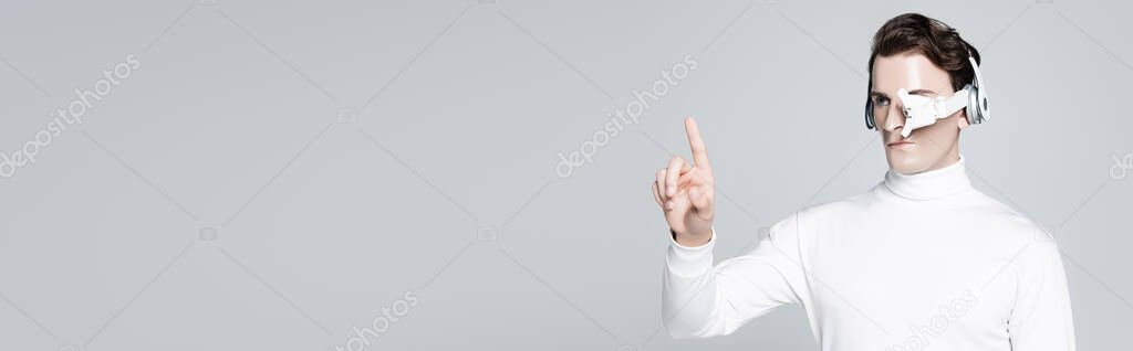 Cyborg in headphones pointing with finger isolated on grey, banner