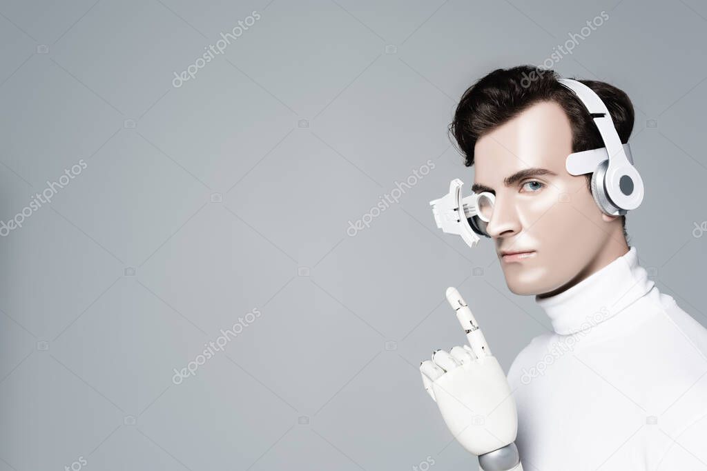 Cyborg man in headphones with artificial hand pointing with finger isolated on grey