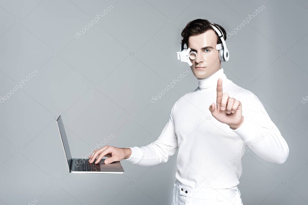 Cyborg in headphones touching something near laptop in air isolated on grey