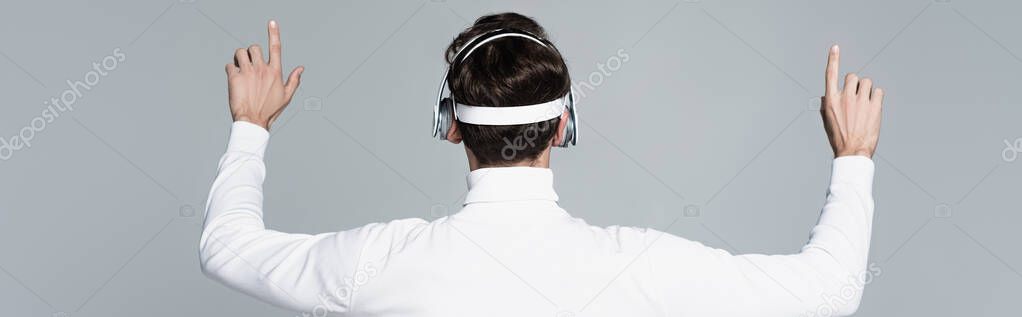 Back view of cyborg in headphones touching something isolated on grey, banner