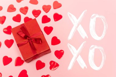 Kırmızı kalplerin üst görüntüsü ve Xoxo harflerinin yanındaki hediye kutusu pembe arka planda.