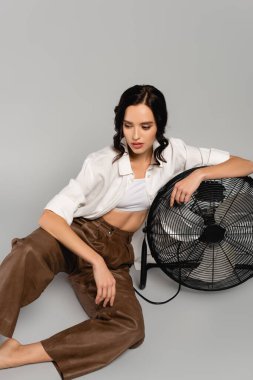 Gri yelpazeye yaslanmış esmer kadın gözlerini kaçırıyor.