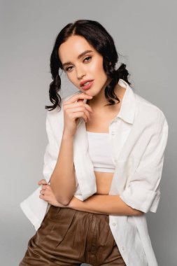 Beyaz bluzlu esmer kadın, gri renkli kameraya bakıyor.