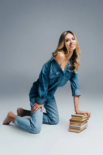 Charming Woman Denim Clothes Naked Shoulder Kneeling Leaning Books Grey — Stock Photo, Image