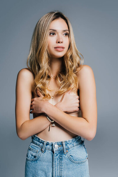 charming topless woman in jeans hiding breasts with hands while looking away isolated on grey