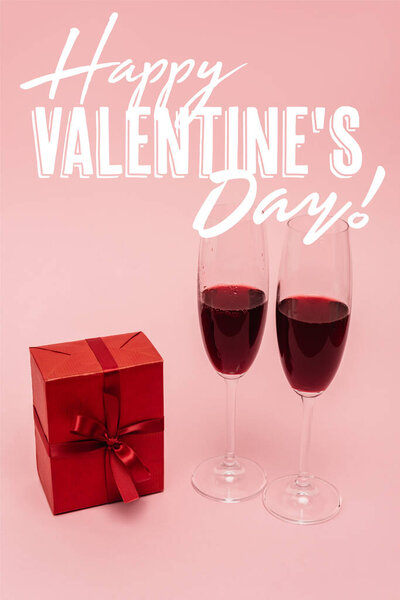 red wine in glasses near gift box and happy valentines day lettering on pink