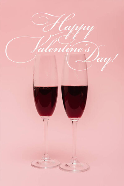 red wine in glasses near happy valentines day lettering on pink