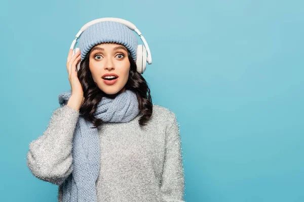 Zaskoczona Brunetka Słuchawkach Ubrana Strój Zimowy Patrząca Odizolowaną Niebiesko Kamerę — Zdjęcie stockowe