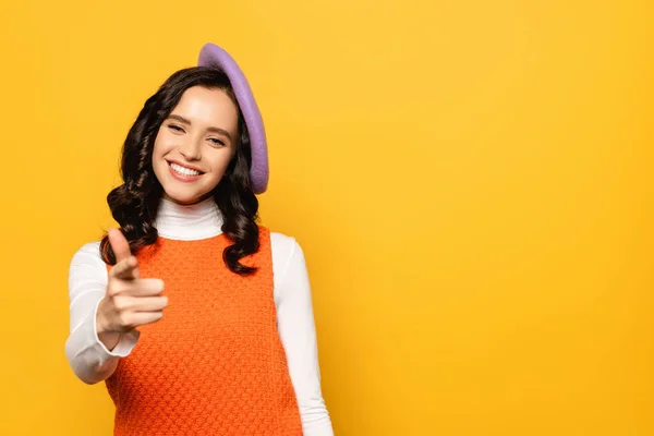 stock image Smiling brunette woman in beret pointing with finger while looking at camera isolated on yellow on blurred foreground