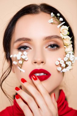 Kırmızı dudaklı ve yüzünde beyaz çiçekler olan genç bir kadın pembe kameraya bakıyor. 