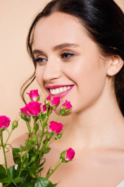 Pembe çiçeklerin yanında gülümseyen neşeli genç kadın. 