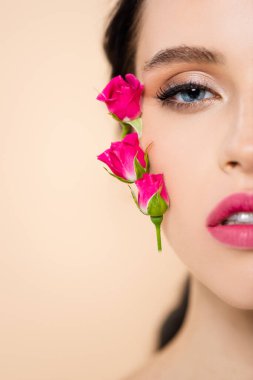 Yüzünde çiçekler olan, pembe izole edilmiş kameraya bakan şehvetli genç kadın görüntüsü. 