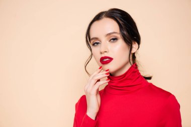 Esmer, kırmızı dudaklı, çenesine dokunan genç bir kadın pembe kameraya bakıyor.