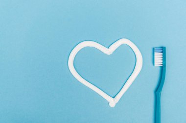 Top view of heart sign from toothpaste and toothbrush on blue background clipart