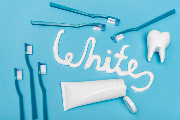 Top view of toothbrushes, tooth model and white lettering from toothpaste on blue background