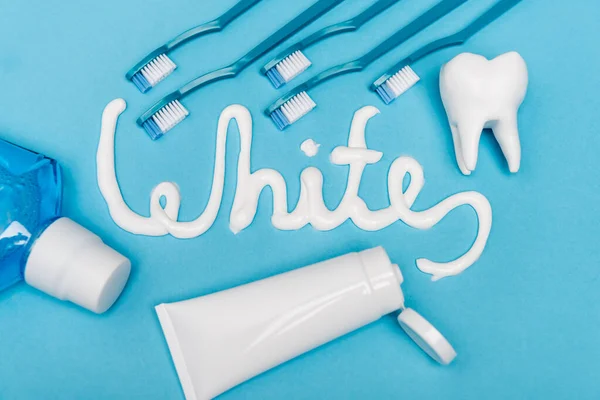 Top view of white lettering from toothpaste, mouthwash and toothbrushes on blue background
