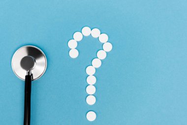 Mavi arka planda haplardan ve steteskoptan gelen soru işaretinin üst görünümü