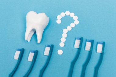 Haplardan, diş modelinden ve mavi arka planda diş fırçasından gelen soru işaretlerinin yüksek açılı görüntüsü