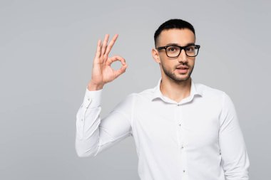 Gözlüklü genç İspanyol menajer gri üzerine izole edilmiş bir jest gösteriyor.