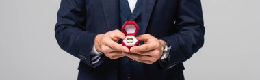 partial view of man in suit holding jewelry box with wedding ring isolated on grey, banner clipart