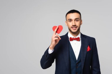 Şık takım elbiseli mutlu İspanyol adam elinde kırmızı kağıt, kalbi gri renkte kesilmiş.