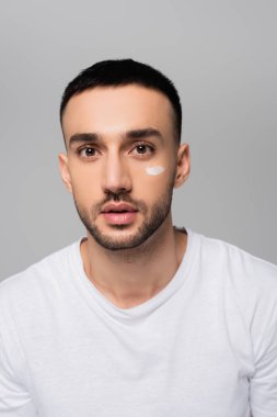 Yüzüne kozmetik krem bulaşmış genç İspanyol adam gri renkli kameraya bakıyor.