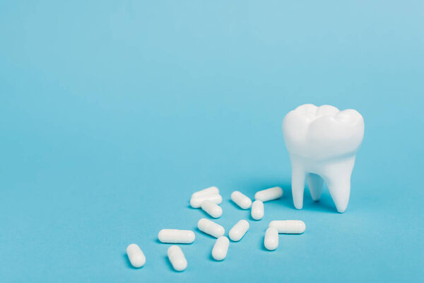 Крупный план белых таблеток и модели зубов на синем фоне