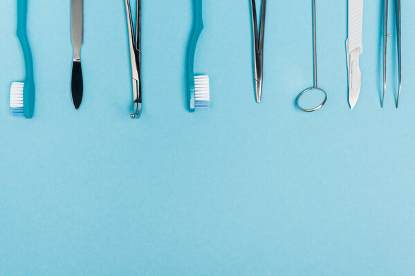 Top view of row of dental tools and toothbrushes on blue background with copy space 