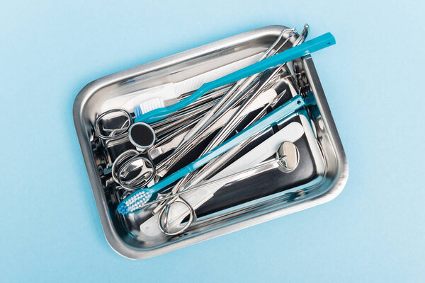 Top view of dental tools and toothbrushes in tray on blue background
