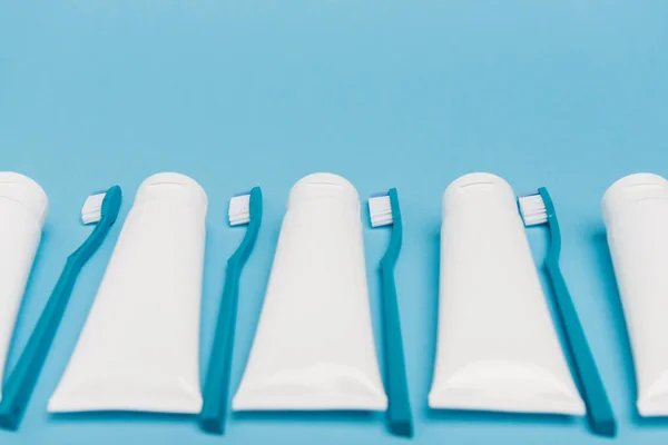 White Tubes Toothpaste Toothbrushes Blurred Foreground Blue Background — Stock Photo, Image