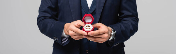 partial view of man in suit holding jewelry box with wedding ring isolated on grey, banner