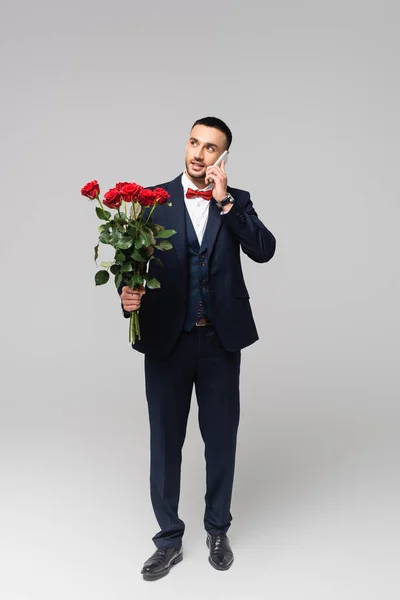 Jovem Hispânico Homem Terno Elegante Falando Smartphone Enquanto Segurando Rosas — Fotografia de Stock