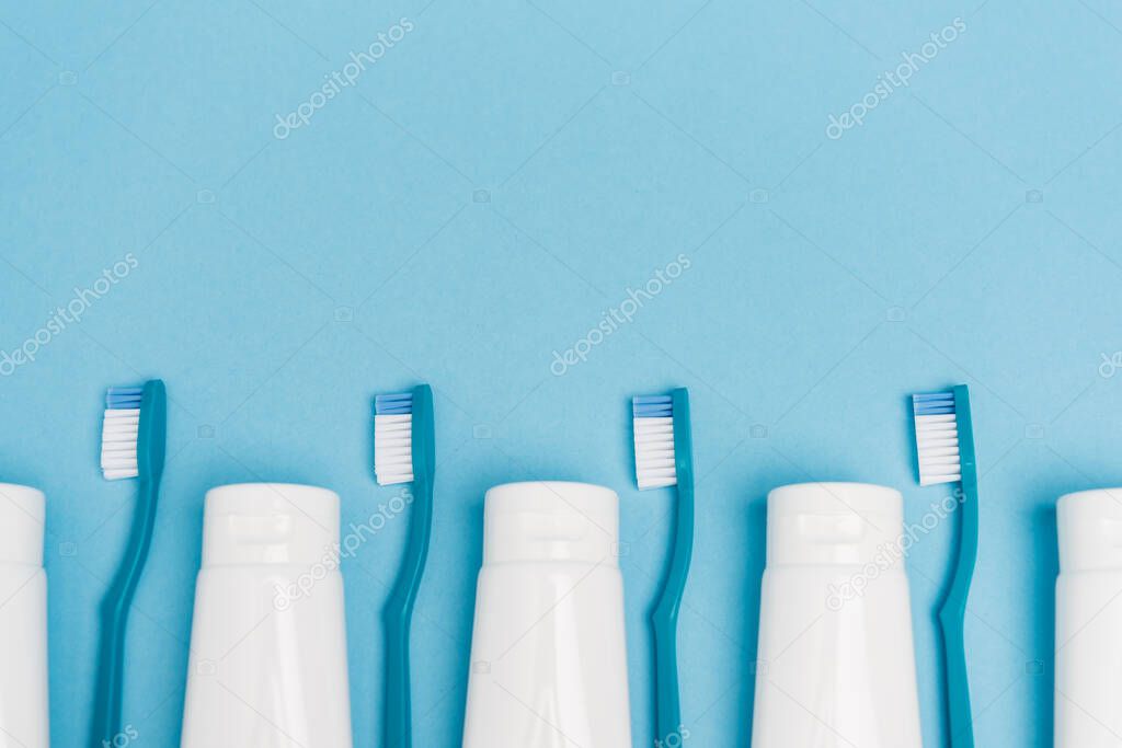 Top view of row of toothbrushes and tubes with toothpaste on blue background