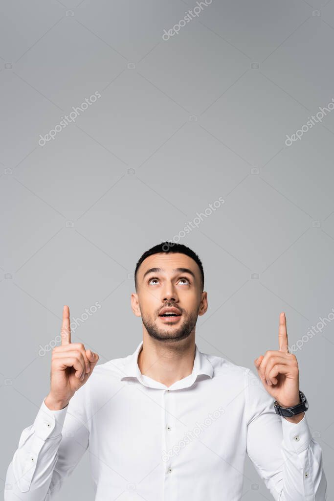 young hispanic businessman looking up and pointing with fingers isolated on grey 