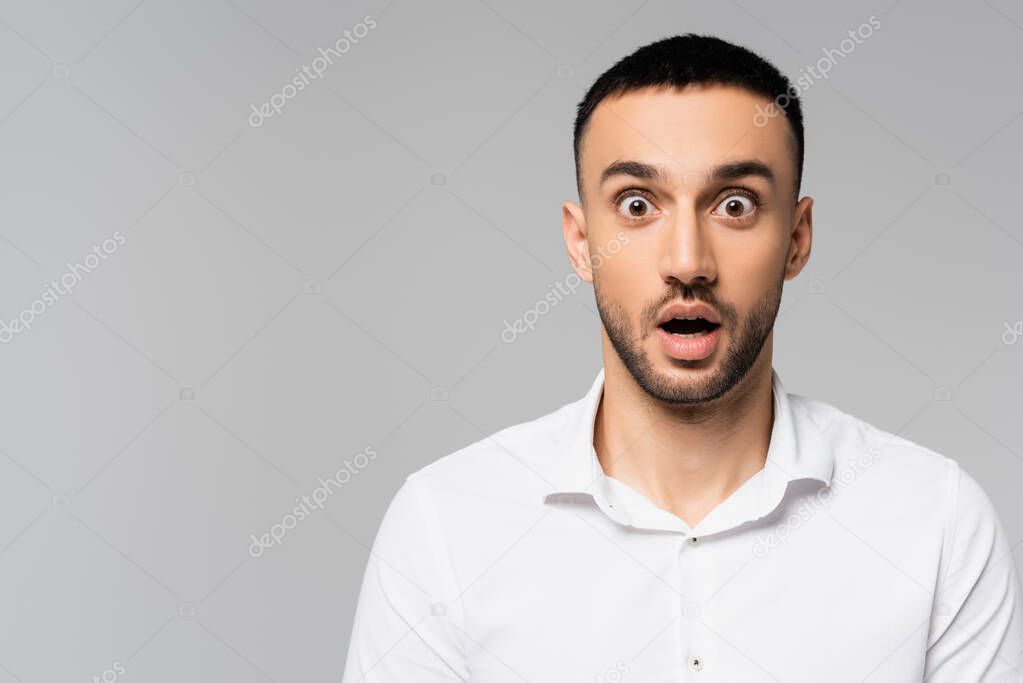 amazed hispanic manager with open mouth and bulging eyes looking at camera isolated on grey