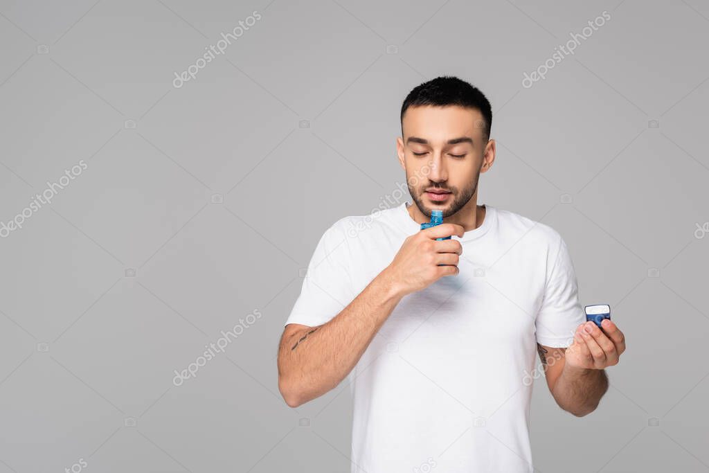 hispanic man smelling cologne water with closed eyes isolated on grey