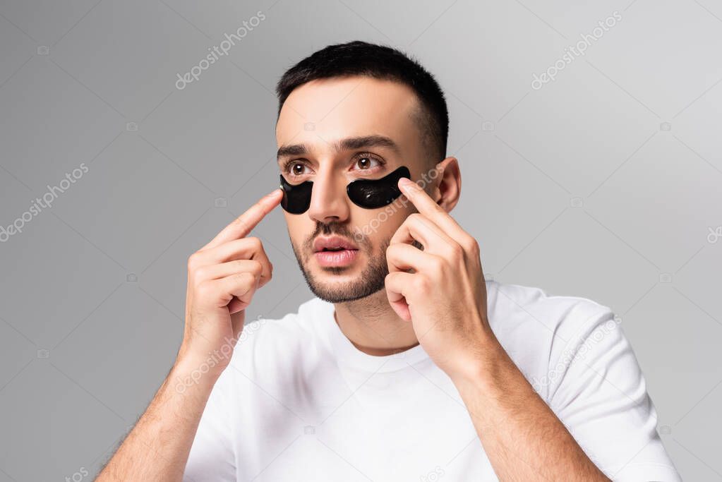 young hispanic man applying eye patches isolated on grey