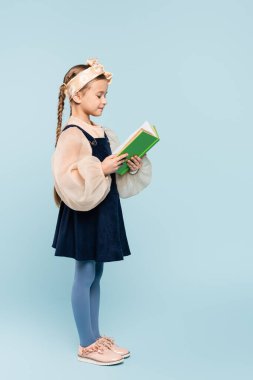 Saçları örgülü, mavi üzerine kitap okuyan küçük bir kız.