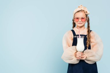 Güneş gözlüklü neşeli kız, elinde bardak ve mavi renkli milkshake var.