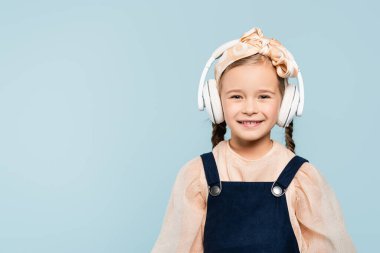 Saç bandı takmış neşeli bir çocuk. Kablosuz kulaklıkları var. Maviyle izole edilmiş müzik dinliyor. 