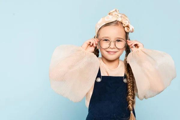 Wesoły Dzieciak Dostosowując Okulary Patrząc Aparat Odizolowany Niebiesko — Zdjęcie stockowe