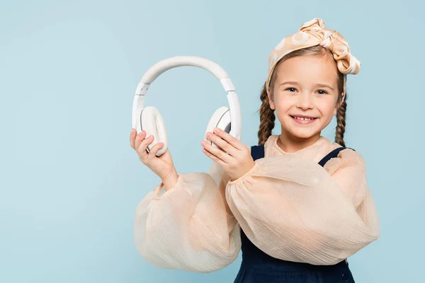 Cheerful Kid Headband Bow Holding Wireless Headphones Isolated Blue — Stock Photo, Image