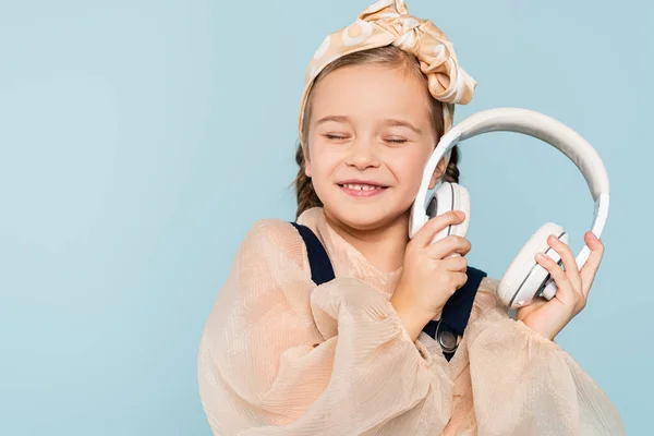 Cheerful Kid Headband Bow Closed Eyes Holding Wireless Headphones Isolated — Stock Photo, Image