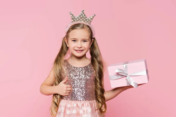 快乐的小女孩 戴着皇冠 手里拿着礼物 带着大拇指 孤零零地躺在粉红上 — 图库照片