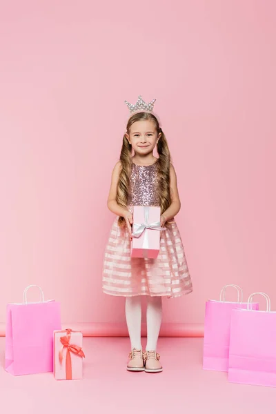 全身上下都是笑容满面的小女孩 头戴皇冠 提着粉红购物袋旁的礼物 — 图库照片