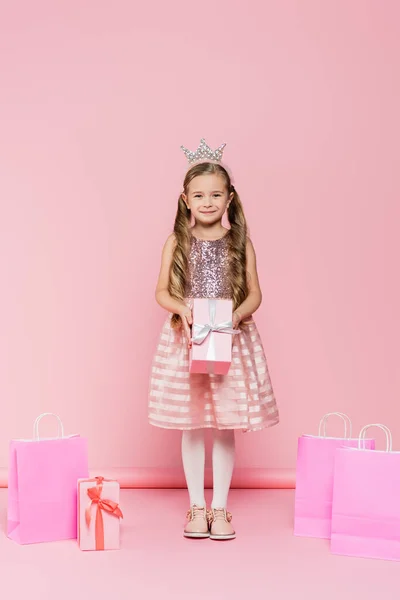 Longitud Completa Niña Sonriente Corona Sosteniendo Presente Cerca Bolsas Compras —  Fotos de Stock