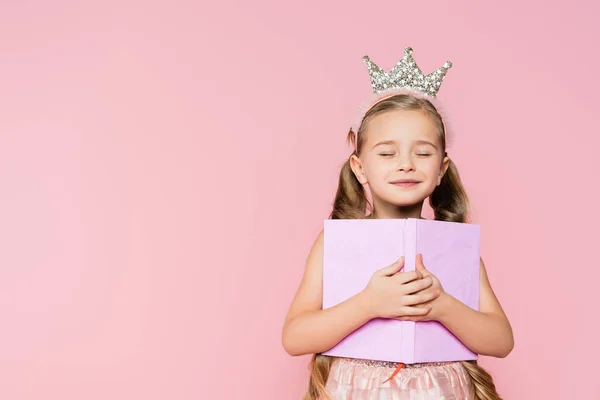 笑着的小女孩 紧闭双眼 头戴皇冠 手里拿着一本粉红色的书 — 图库照片