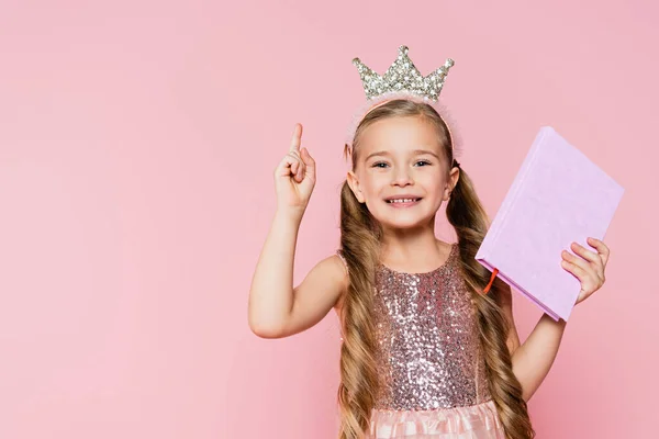 Glimlachend Klein Meisje Kroon Holding Boek Wijzen Met Vinger Geïsoleerd — Stockfoto