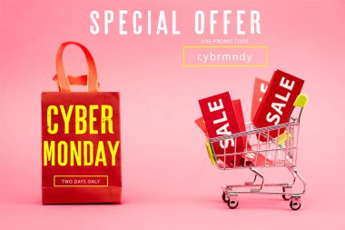red tags with sale in shopping trolley near paper bag with cyber monday lettering on pink clipart